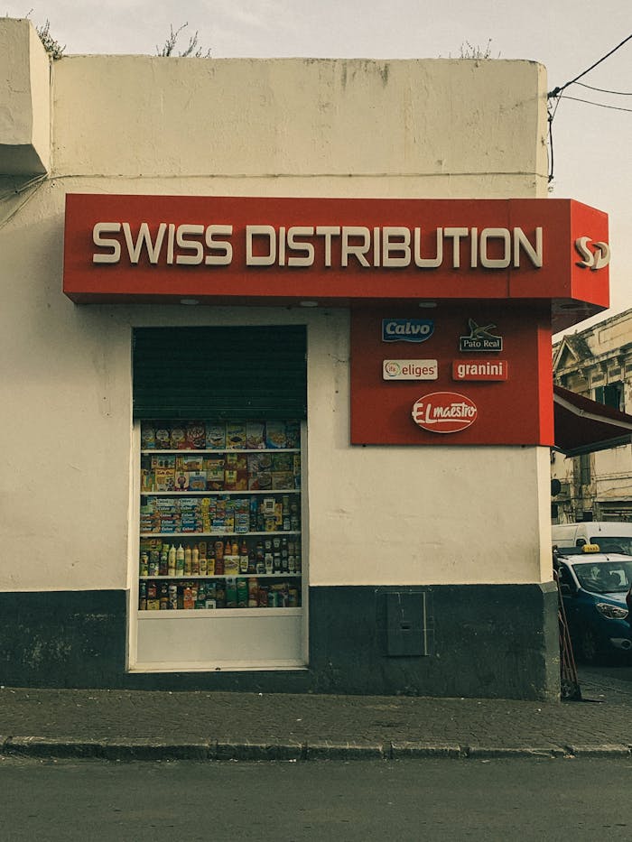 services-03 Street view of a store with a prominent Swiss Distribution sign and product display.