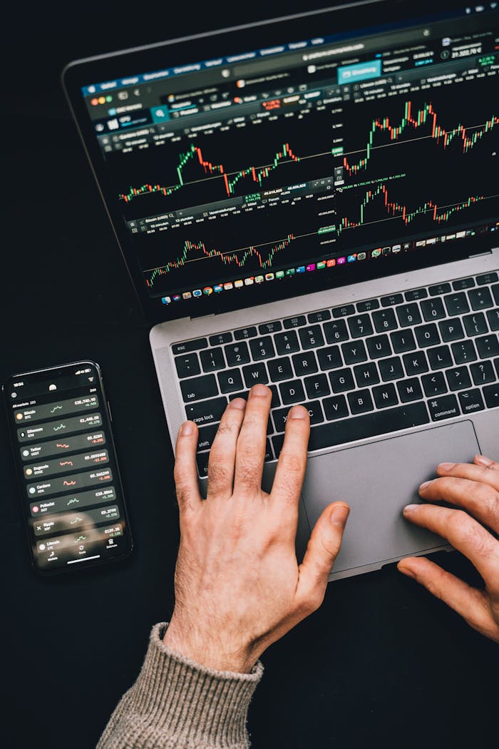 services-04 Hands typing on a laptop with cryptocurrency charts and smartphone display in view, focusing on digital finance.